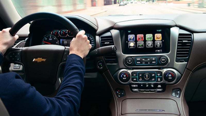Interior view of the Chevrolet Suburban showing the dashboard, touchscreen display, and a driver’s hands on the steering wheel.