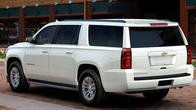 A white Chevrolet Suburban parked outside a modern building, viewed from the rear driver-side angle.