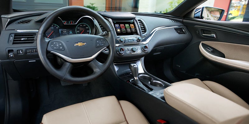 Front interior view of the 2019 Chevrolet Impala with beige leather seats, touchscreen infotainment system, and chrome accents