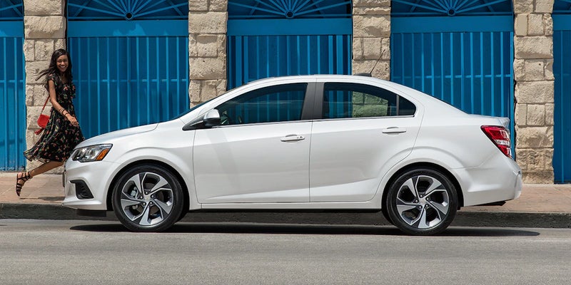 Chevrolet Sonic parked near a building with a happy woman nearby