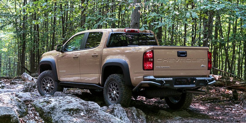 Beige 2021 Chevrolet Colorado navigating rocky terrain in a wooded area