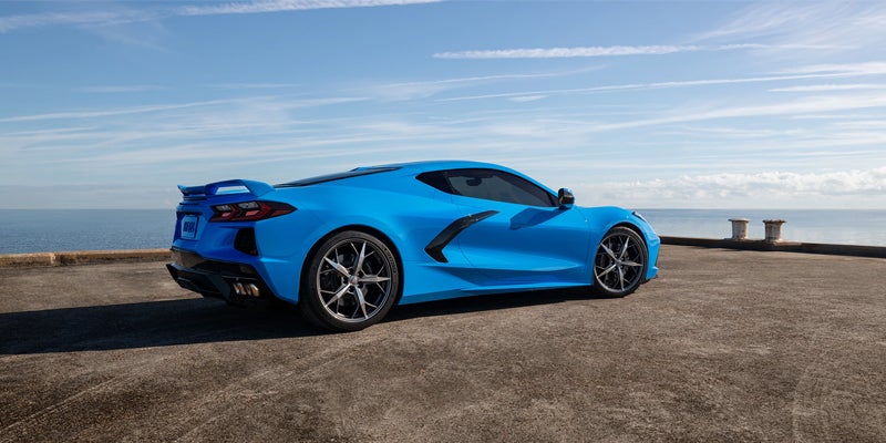 Rear side view of a blue Chevrolet Corvette parked near the ocean under a bright sky