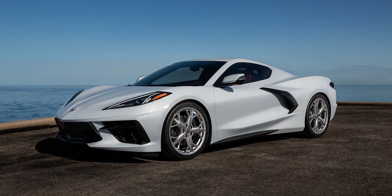 Front side view of a white Chevrolet Corvette parked by the water under clear skies