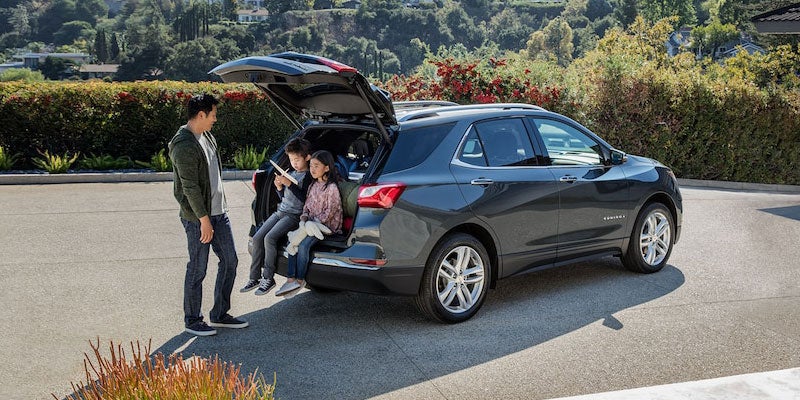 A family sitting on the rear bumper of a 2021 Chevrolet Equinox with the liftgate open in a suburban driveway.