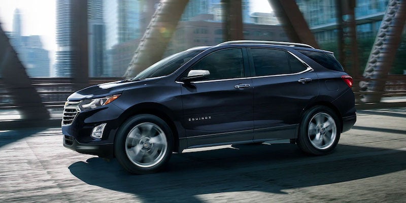 Side view of a navy blue 2021 Chevy Equinox driving across a bridge in an urban setting.