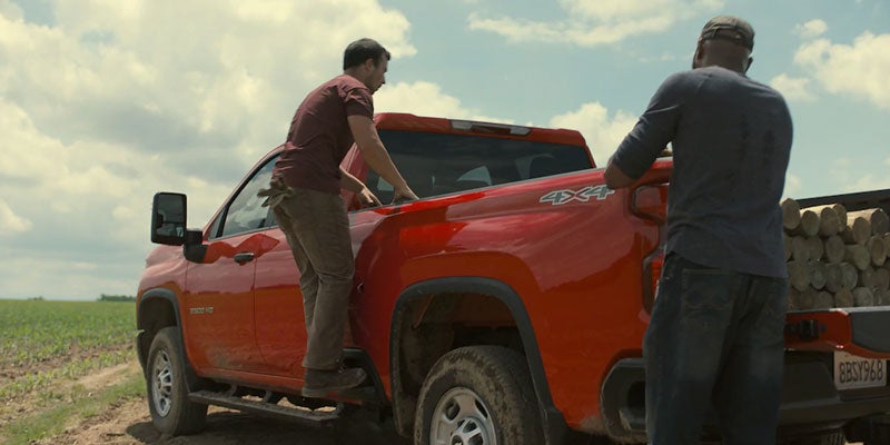 Red Chevrolet Silverado parked on a road, with two men loading wooden logs into the truck bed