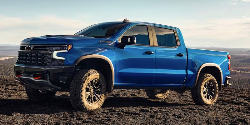Side profile of a blue 2024 Chevrolet Silverado 1500 parked on a dirt landscape