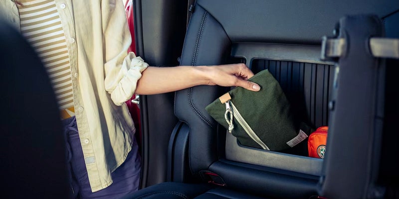 Person placing a green pouch into rear seatback storage compartment of a Chevy Silverado 1500.