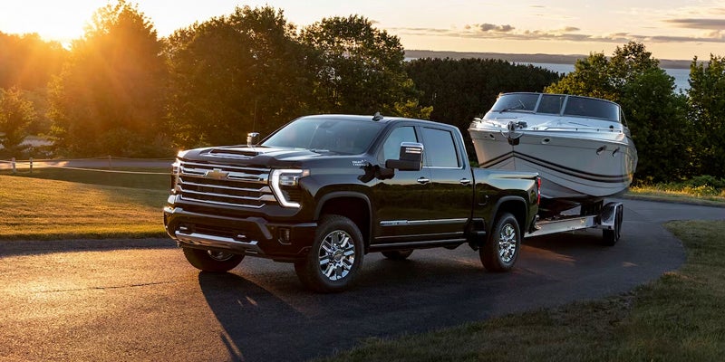 2024 Chevrolet Silverado HD towing a boat at sunset, highlighting its powerful towing capacity and rugged utility.