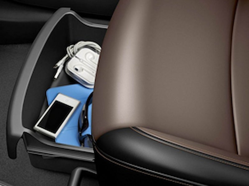 Under-seat storage tray in the 2016 Chevrolet Trax holding various personal items like phone and charger.