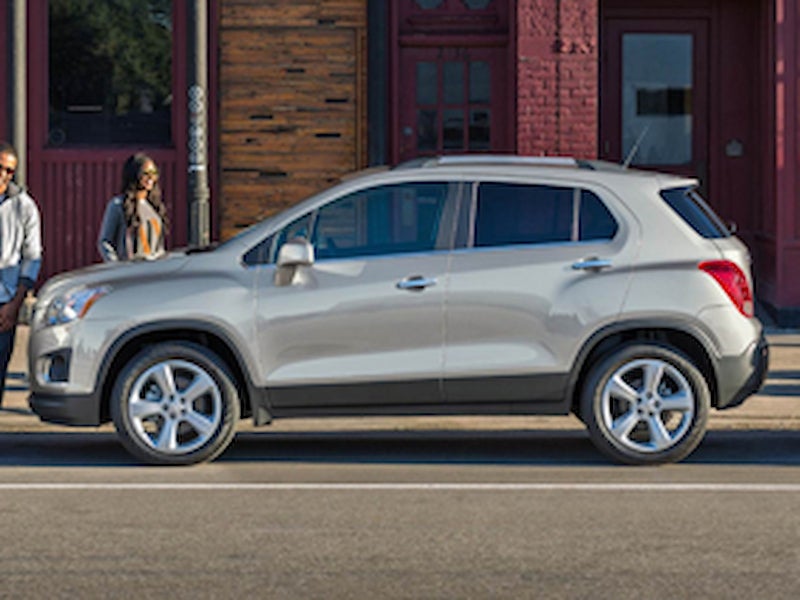 Side profile of a silver 2016 Chevrolet Trax parked on a city street with pedestrians nearby.