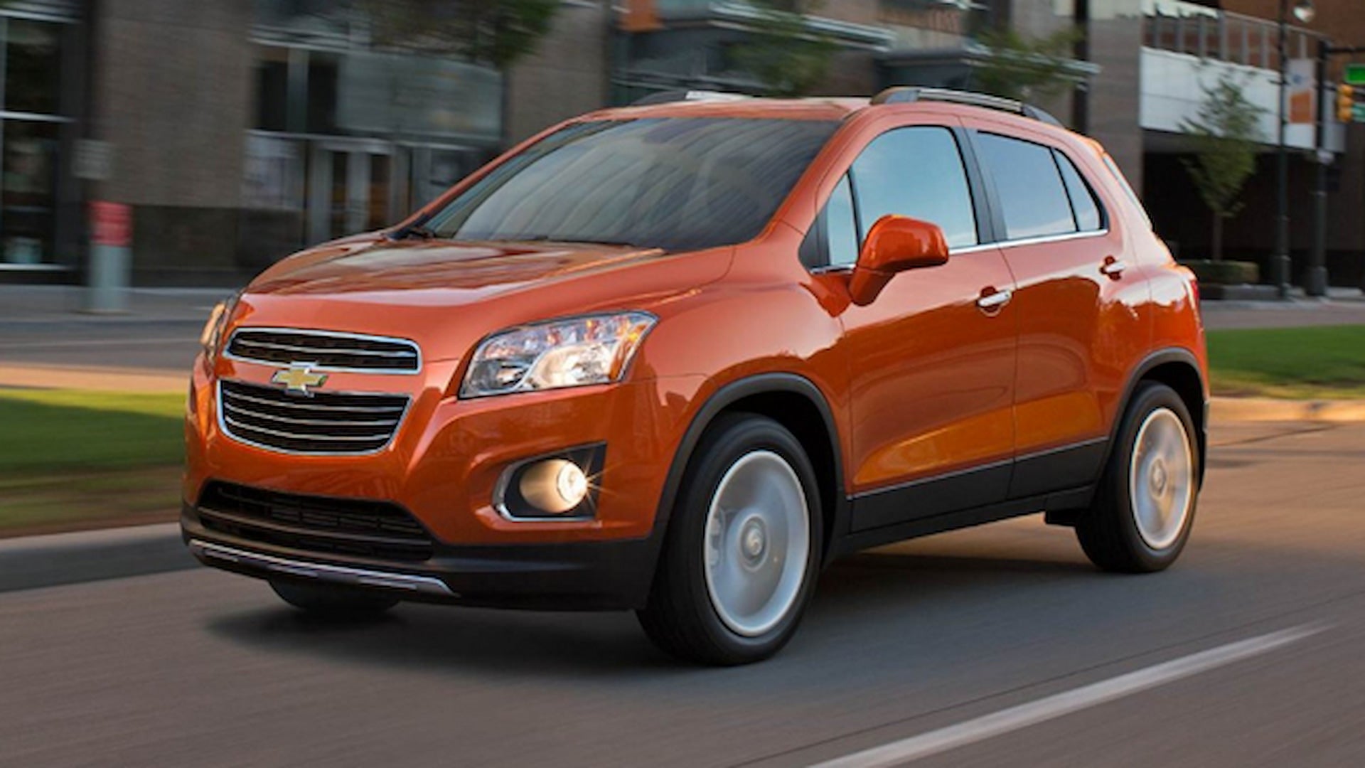 2016 Chevrolet Trax in orange driving through a city street, showcasing its compact SUV design.