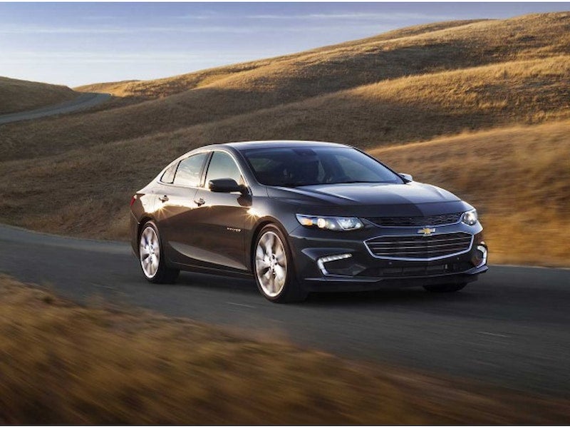Front view of the 2017 Chevrolet Malibu driving on a curvy road surrounded by golden hills at sunset.