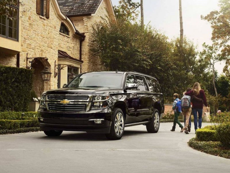 Black 2017 Chevrolet Suburban parked in a residential driveway as a family walks nearby